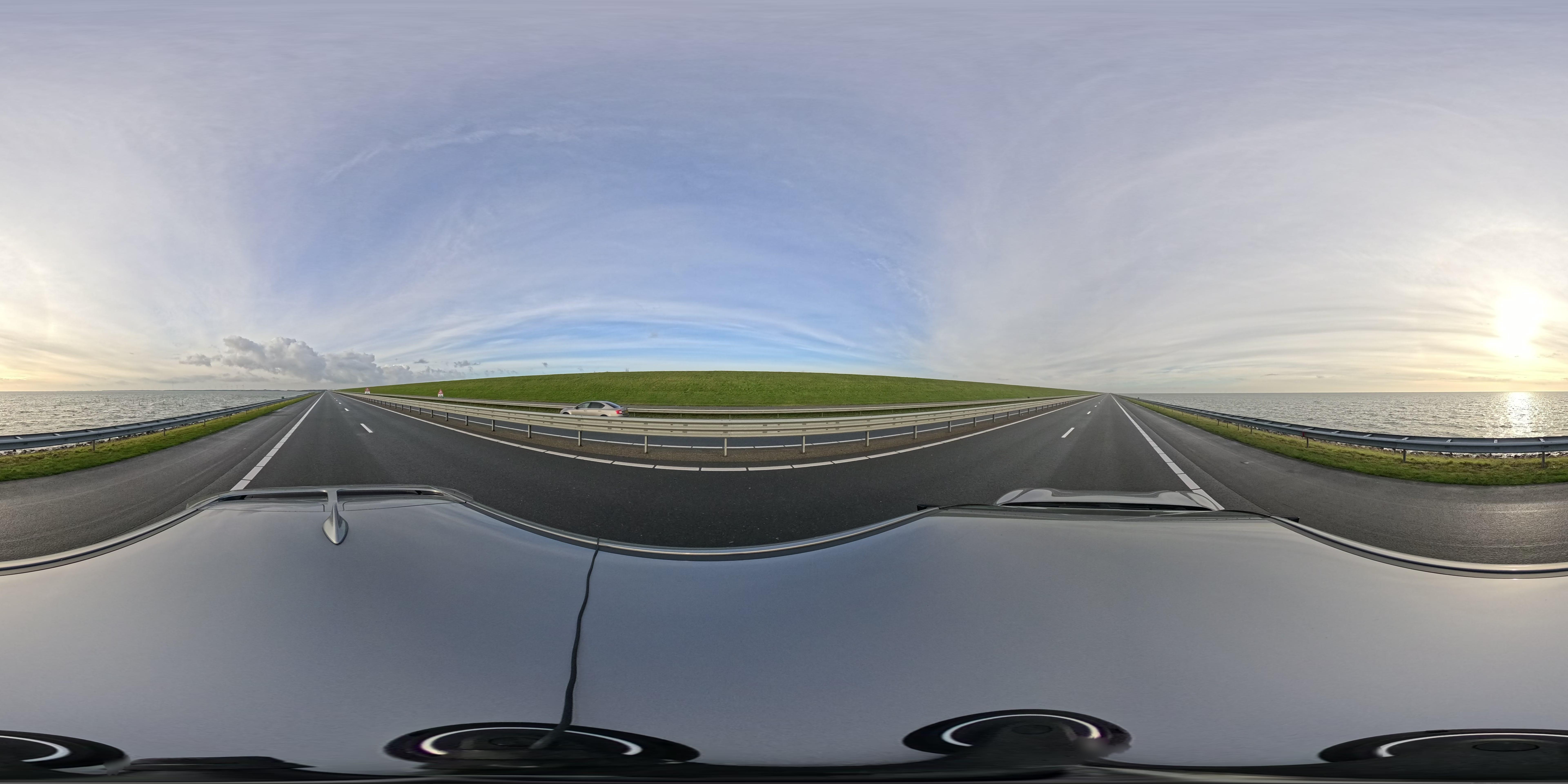 Equirectangular road panorama with water, sky, guardrails and a vehicle roof at the bottom