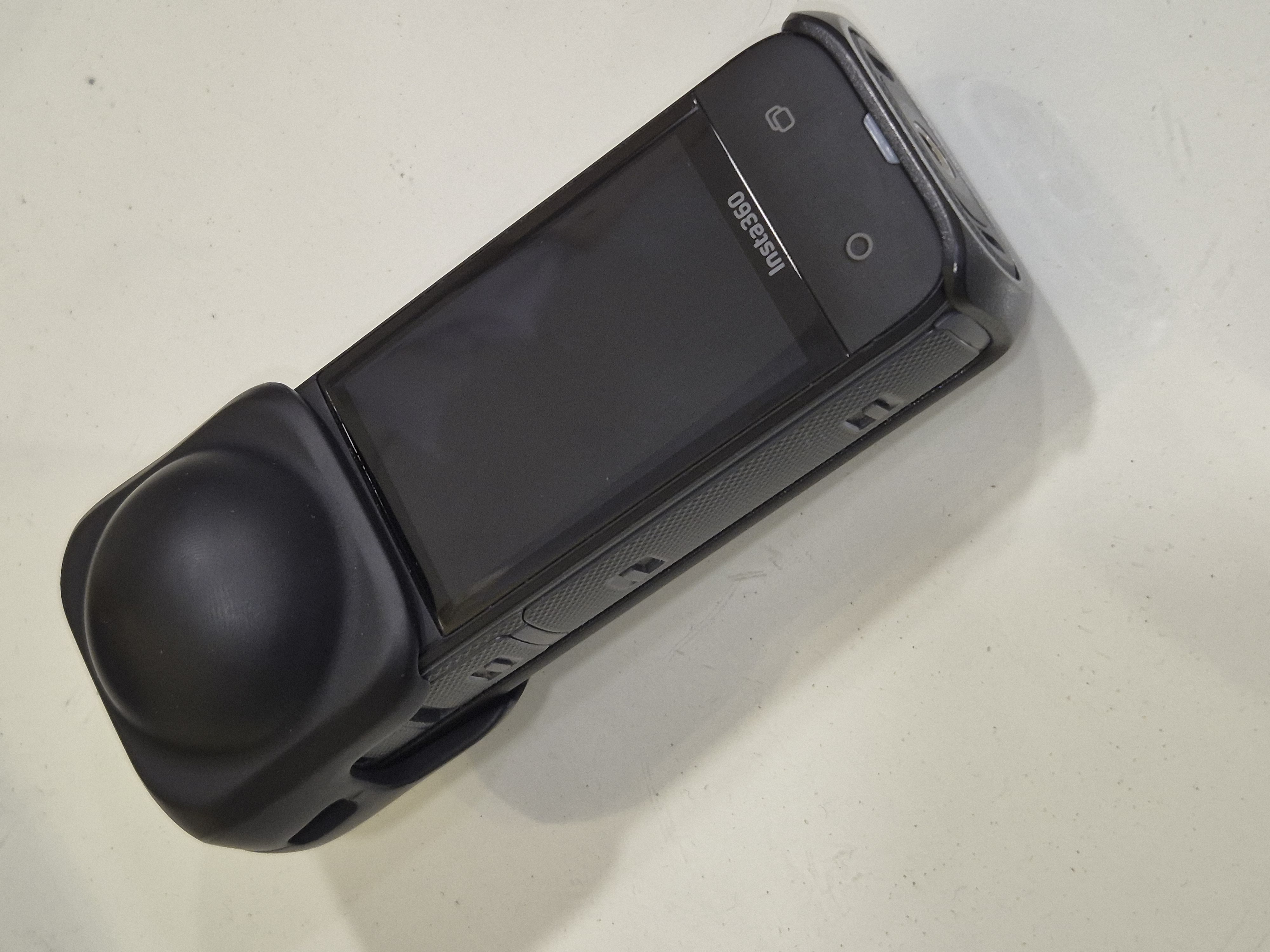 Insta360 X4 resting on a white surface with its lens cap fitted and touchscreen visible
