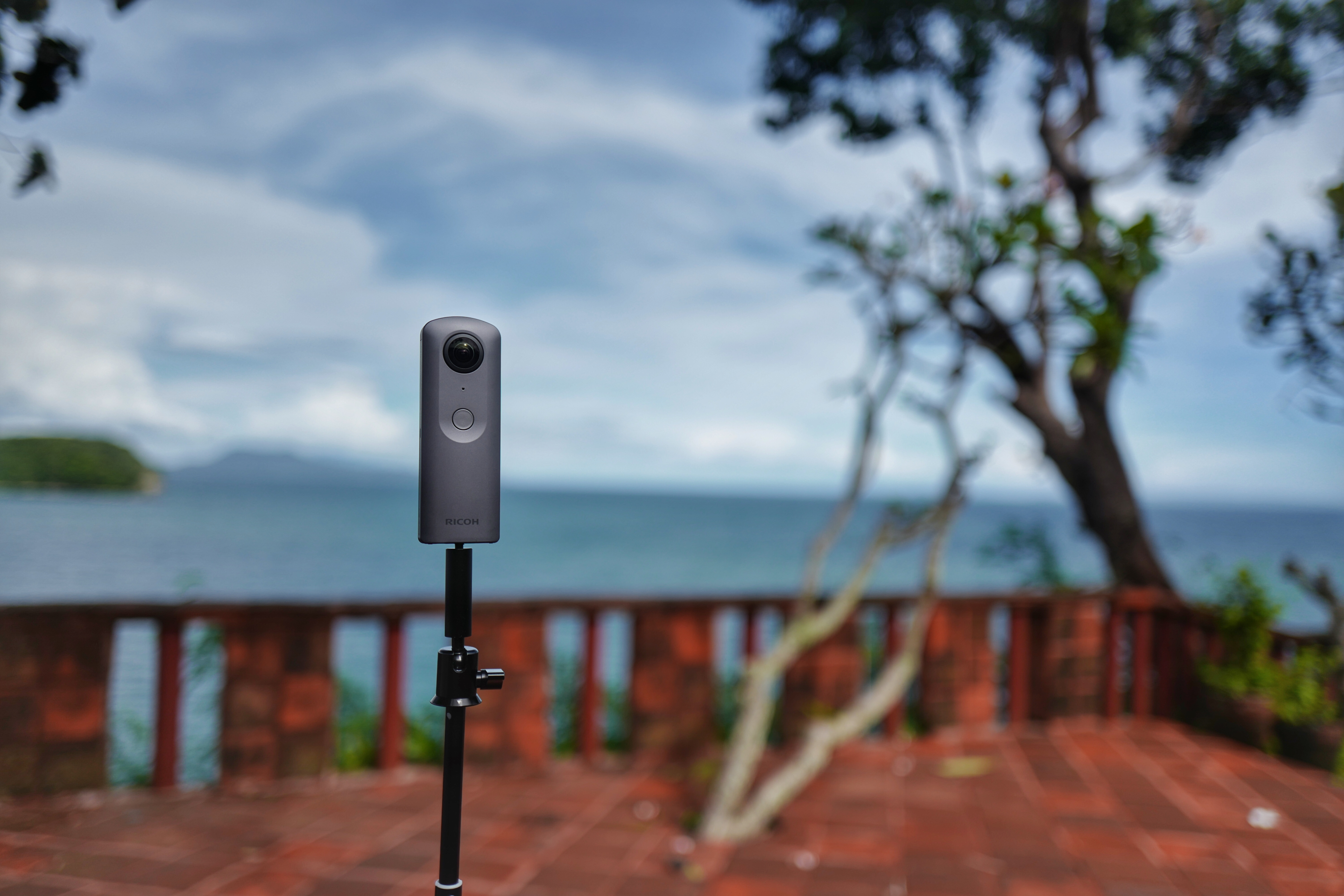 Ricoh Theta V mounted on a slim support beside a terrace overlooking water