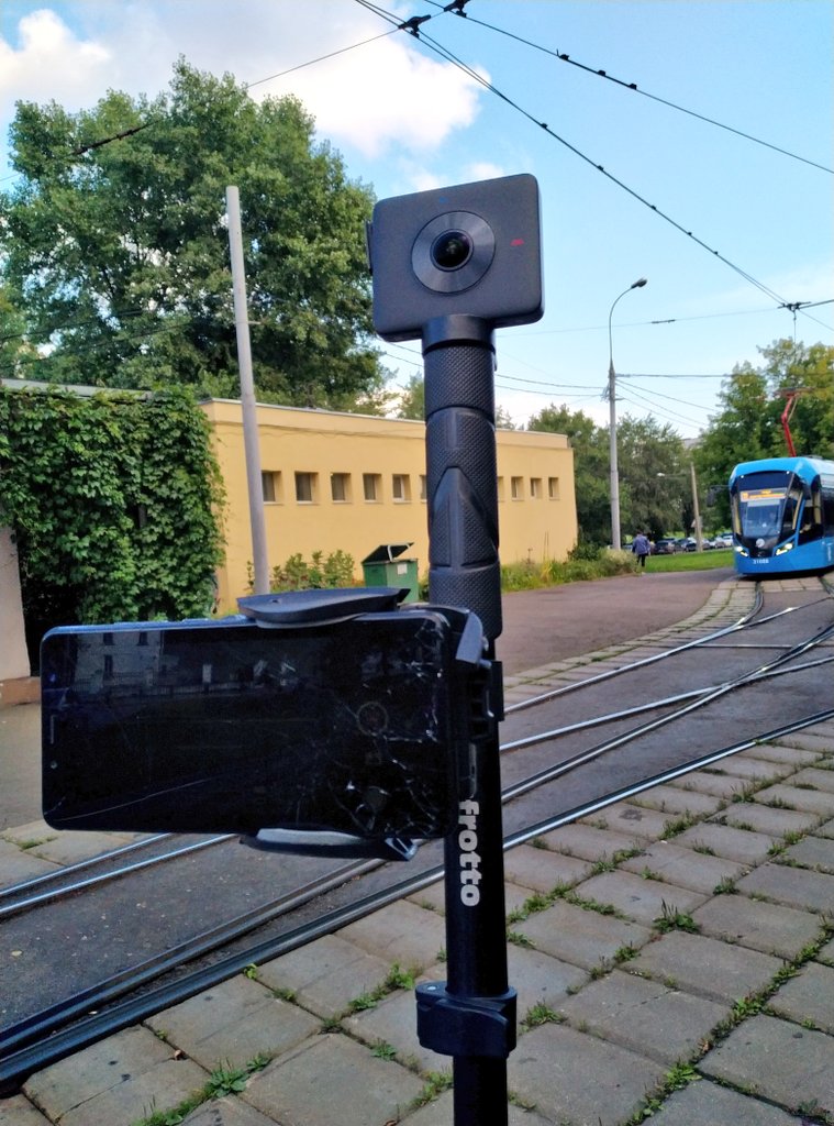 Square black Xiaomi Mijia 360 camera mounted on a pole above a smartphone beside tram tracks